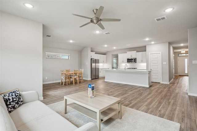 living room featuring sink, ceiling fan, and light wood-type flooring