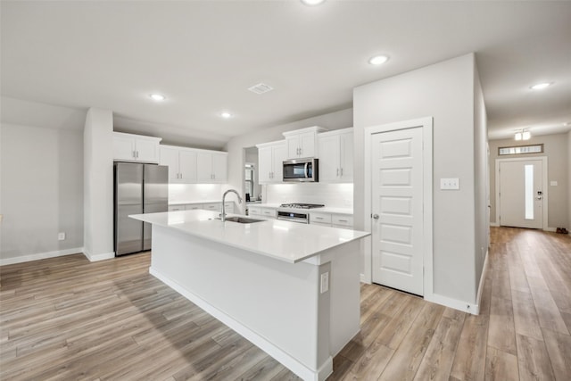 kitchen with sink, white cabinetry, light hardwood / wood-style flooring, appliances with stainless steel finishes, and an island with sink