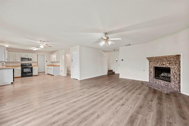 unfurnished living room with sink, a brick fireplace, ceiling fan, and light wood-type flooring