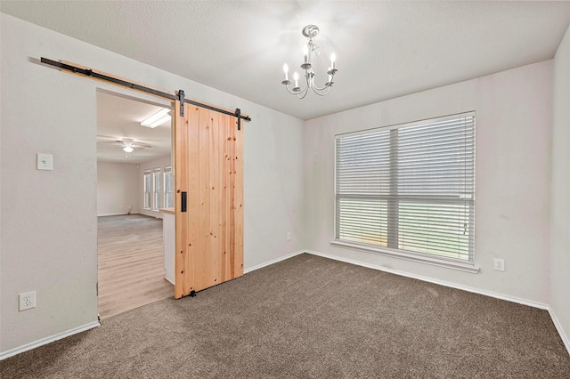 carpeted spare room featuring a barn door, a textured ceiling, and an inviting chandelier