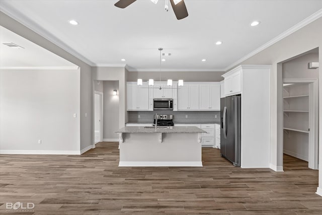 kitchen featuring a breakfast bar area, decorative light fixtures, a center island with sink, stainless steel appliances, and white cabinets