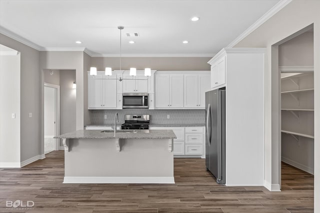 kitchen featuring white cabinetry, stainless steel appliances, light stone counters, a center island with sink, and decorative light fixtures