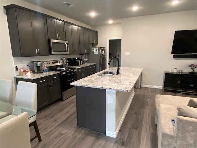 kitchen featuring sink, stainless steel appliances, dark wood-type flooring, light stone countertops, and a kitchen island with sink