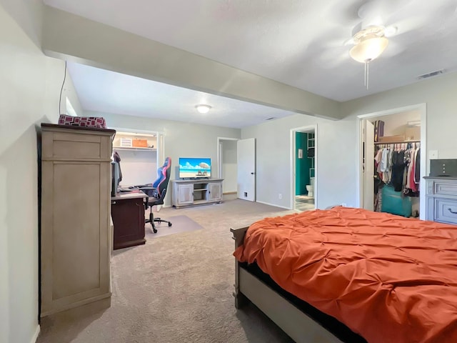 bedroom with connected bathroom, a walk in closet, light colored carpet, ceiling fan, and a closet