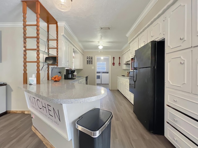 kitchen featuring black fridge, white cabinets, washer and clothes dryer, and kitchen peninsula