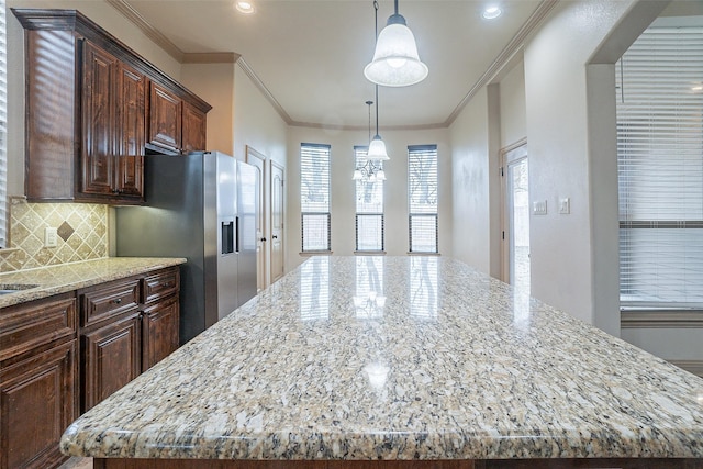 kitchen featuring hanging light fixtures, stainless steel refrigerator with ice dispenser, light stone countertops, and a large island