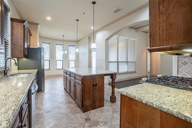 kitchen featuring hanging light fixtures, sink, light stone countertops, and a center island