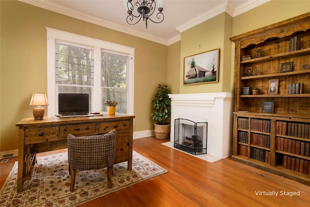 office space with a notable chandelier, a brick fireplace, crown molding, and hardwood / wood-style floors