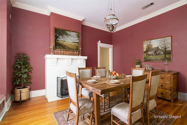 dining space featuring hardwood / wood-style flooring, ornamental molding, a brick fireplace, and an inviting chandelier