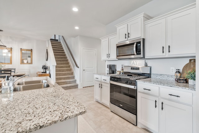 kitchen with appliances with stainless steel finishes, sink, white cabinets, and light stone counters