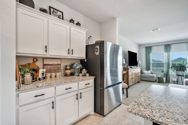 kitchen with white cabinetry, light stone counters, stainless steel refrigerator, and light tile patterned flooring