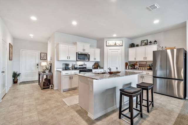 kitchen with stone counters, sink, white cabinets, a kitchen island with sink, and stainless steel appliances