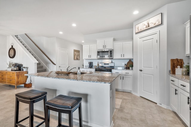 kitchen with white cabinetry, sink, a kitchen breakfast bar, stainless steel appliances, and light stone countertops