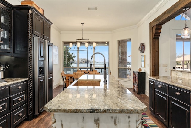 kitchen featuring ornamental molding, paneled built in refrigerator, hanging light fixtures, and a center island with sink