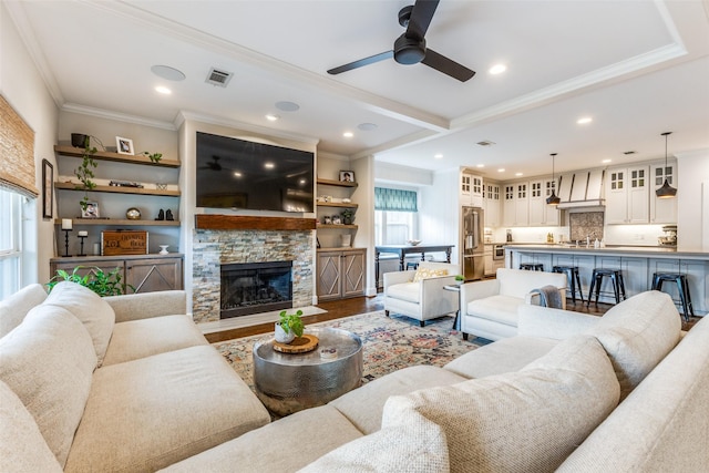 living room featuring crown molding, hardwood / wood-style flooring, ceiling fan, a stone fireplace, and beamed ceiling