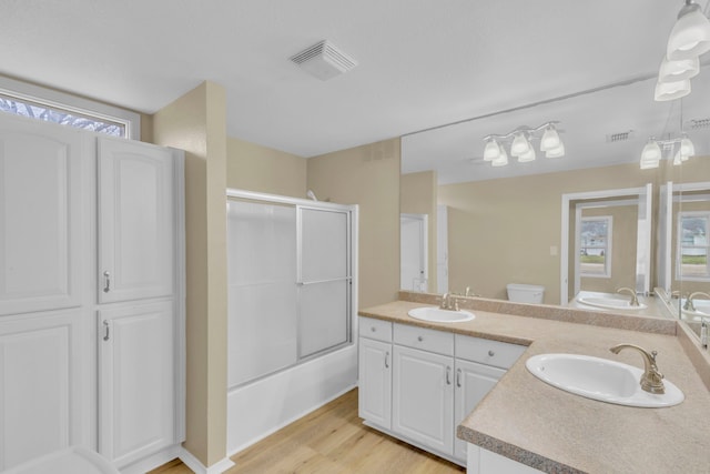 full bathroom featuring vanity, hardwood / wood-style flooring, enclosed tub / shower combo, and toilet