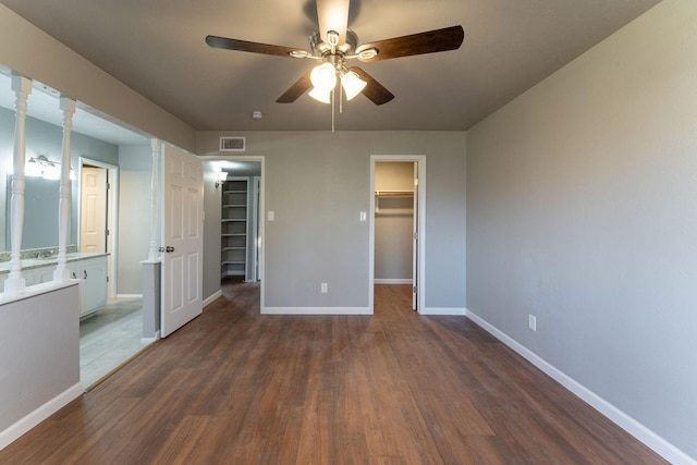 unfurnished bedroom featuring dark wood-type flooring, a walk in closet, ceiling fan, and a closet