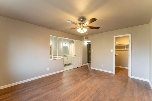 unfurnished bedroom featuring ensuite bath, ceiling fan, hardwood / wood-style floors, a walk in closet, and a closet