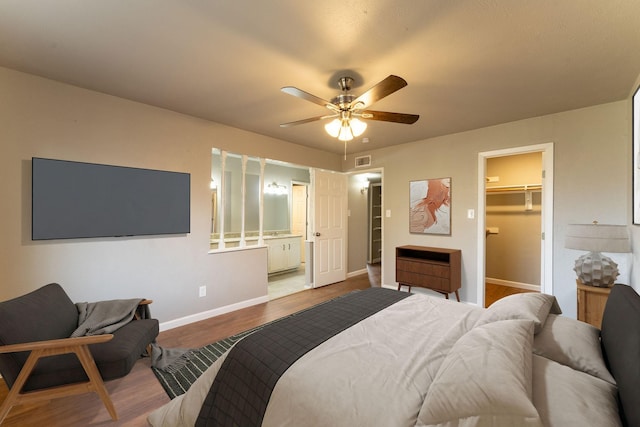 bedroom featuring light hardwood / wood-style flooring, ceiling fan, ensuite bathroom, a spacious closet, and a closet