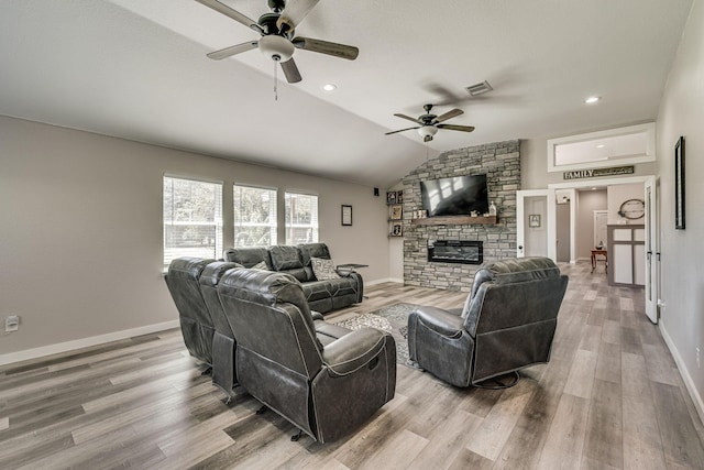 living room featuring a stone fireplace, vaulted ceiling, light hardwood / wood-style floors, and ceiling fan