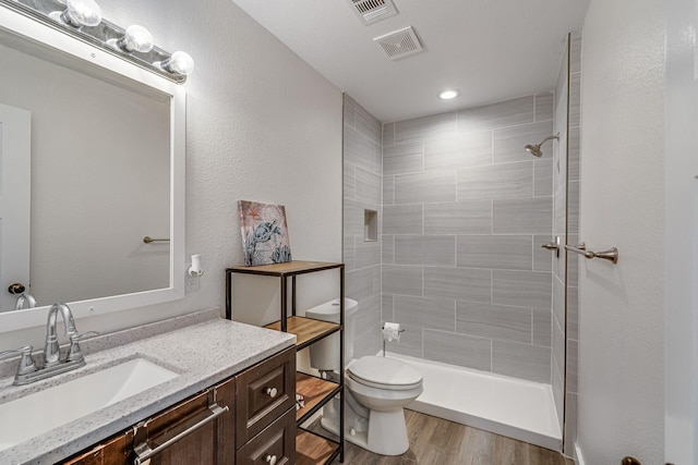 bathroom with wood-type flooring, a tile shower, vanity, and toilet