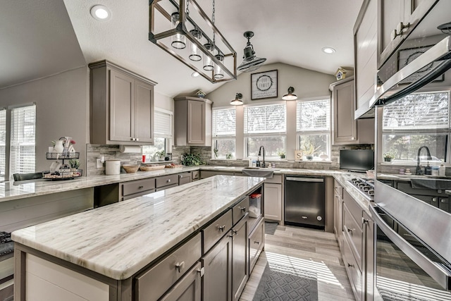 kitchen featuring a center island, vaulted ceiling, appliances with stainless steel finishes, light stone countertops, and decorative backsplash