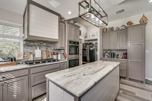 kitchen featuring gray cabinetry, decorative light fixtures, a center island, appliances with stainless steel finishes, and light hardwood / wood-style floors