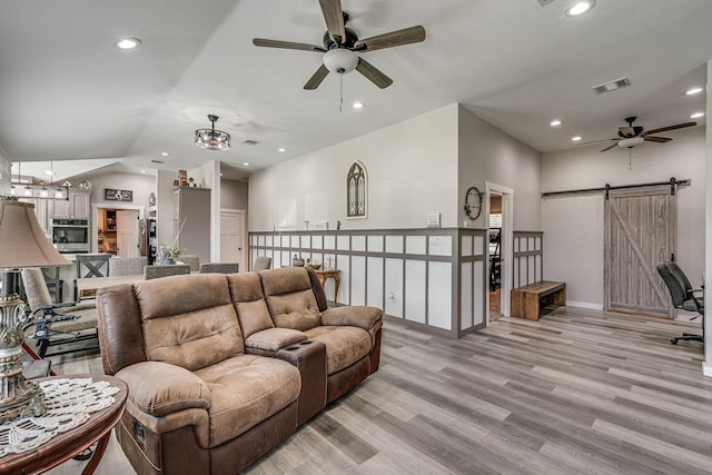 living room featuring vaulted ceiling, a barn door, ceiling fan, and light wood-type flooring