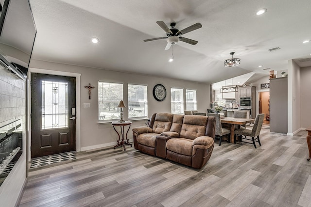 living room with vaulted ceiling, a textured ceiling, light wood-type flooring, ceiling fan, and a tiled fireplace