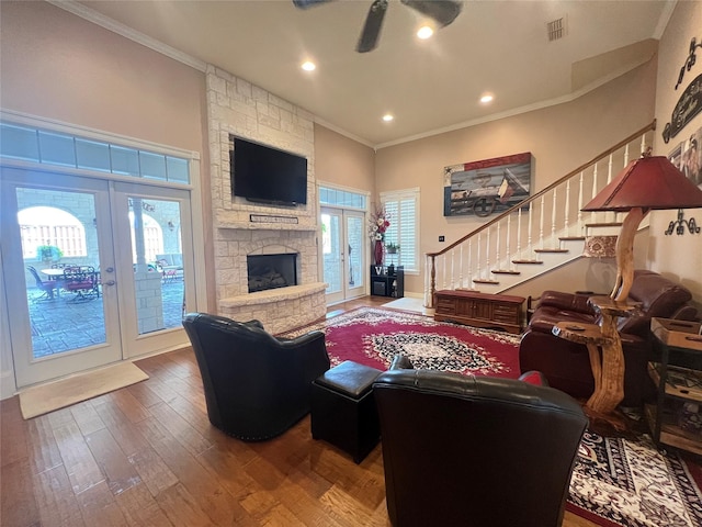 living room featuring crown molding, ceiling fan, wood-type flooring, a stone fireplace, and french doors