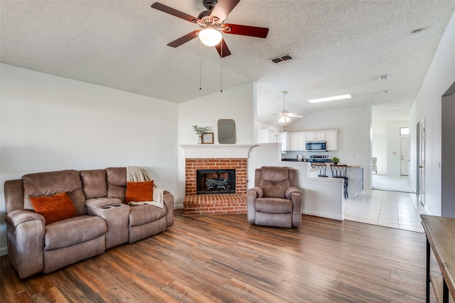 living room with lofted ceiling, a textured ceiling, hardwood / wood-style flooring, ceiling fan, and a fireplace