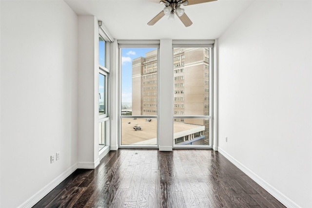 spare room with dark wood-type flooring, a wall of windows, and ceiling fan