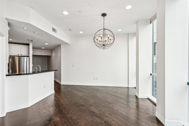 unfurnished living room with dark wood-type flooring, sink, and an inviting chandelier