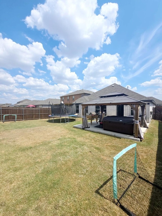 back of house featuring a lawn, a trampoline, a hot tub, a gazebo, and a patio area