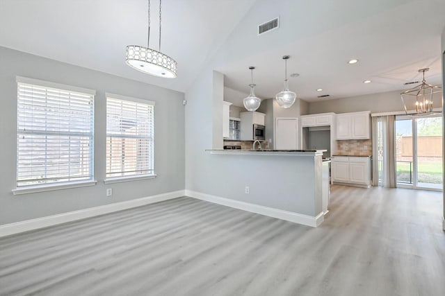 kitchen with stainless steel microwave, tasteful backsplash, white cabinetry, kitchen peninsula, and an inviting chandelier