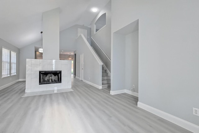 unfurnished living room featuring a tiled fireplace, vaulted ceiling, and light wood-type flooring