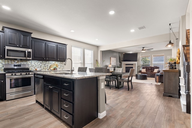 kitchen featuring appliances with stainless steel finishes, an island with sink, sink, light stone counters, and plenty of natural light