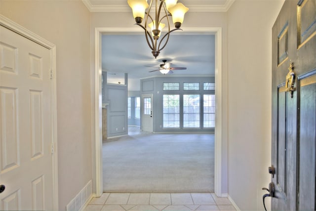 carpeted entrance foyer with ornamental molding and ceiling fan with notable chandelier