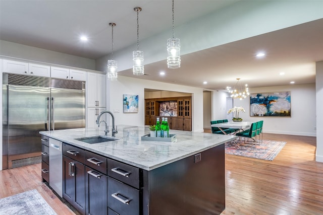 kitchen with appliances with stainless steel finishes, white cabinetry, sink, a kitchen island with sink, and light wood-type flooring