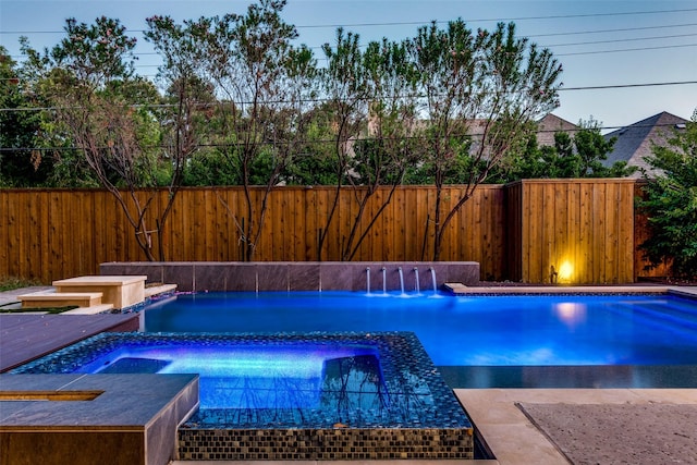 pool at dusk featuring an in ground hot tub and pool water feature