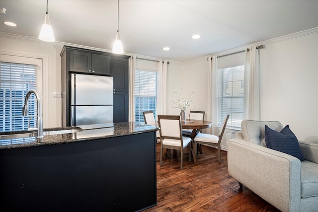 kitchen featuring sink, decorative light fixtures, dark stone countertops, dark hardwood / wood-style floors, and stainless steel fridge