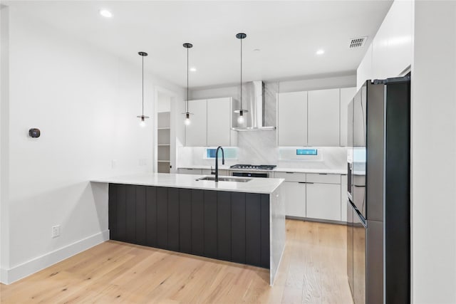 kitchen featuring wall chimney exhaust hood, decorative light fixtures, sink, and white cabinets