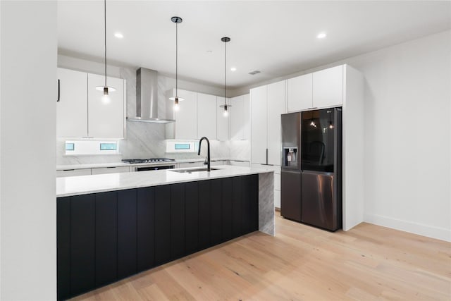 kitchen with white cabinetry, sink, refrigerator with ice dispenser, hanging light fixtures, and wall chimney exhaust hood