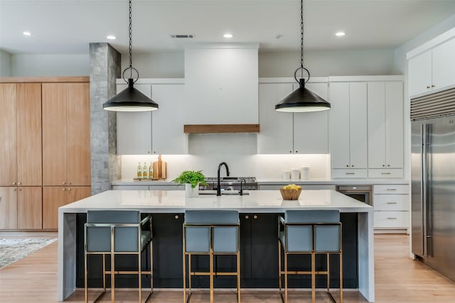 kitchen featuring white cabinetry, decorative light fixtures, stainless steel built in fridge, and a center island with sink