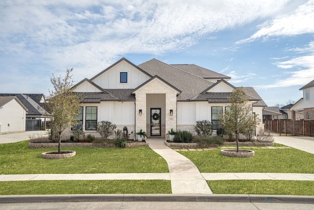 view of front of property with a shingled roof, fence, board and batten siding, and a front yard