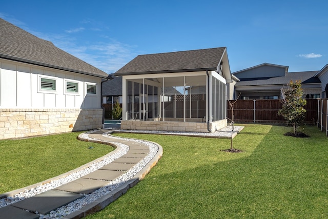 rear view of house featuring roof with shingles, fence, a yard, and a sunroom