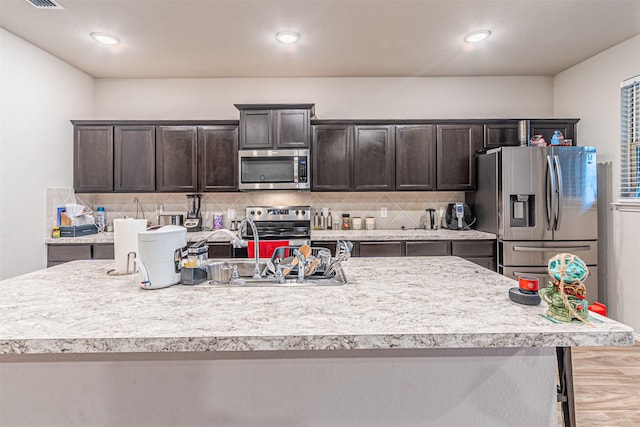 kitchen with a kitchen island with sink, dark brown cabinets, stainless steel appliances, and tasteful backsplash