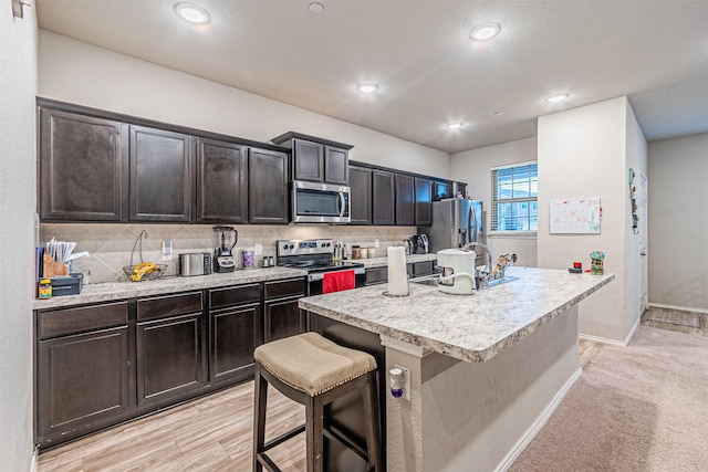 kitchen with decorative backsplash, stainless steel appliances, a kitchen breakfast bar, and a center island with sink