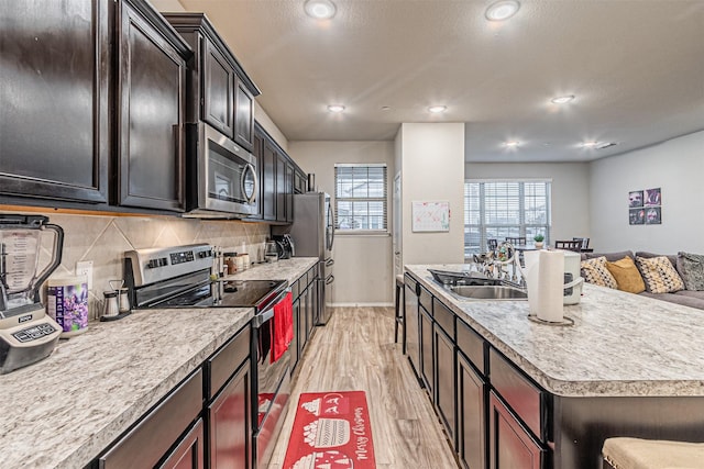 kitchen featuring sink, light hardwood / wood-style flooring, appliances with stainless steel finishes, a center island with sink, and decorative backsplash