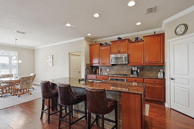 kitchen with appliances with stainless steel finishes, a kitchen island with sink, sink, and dark hardwood / wood-style flooring